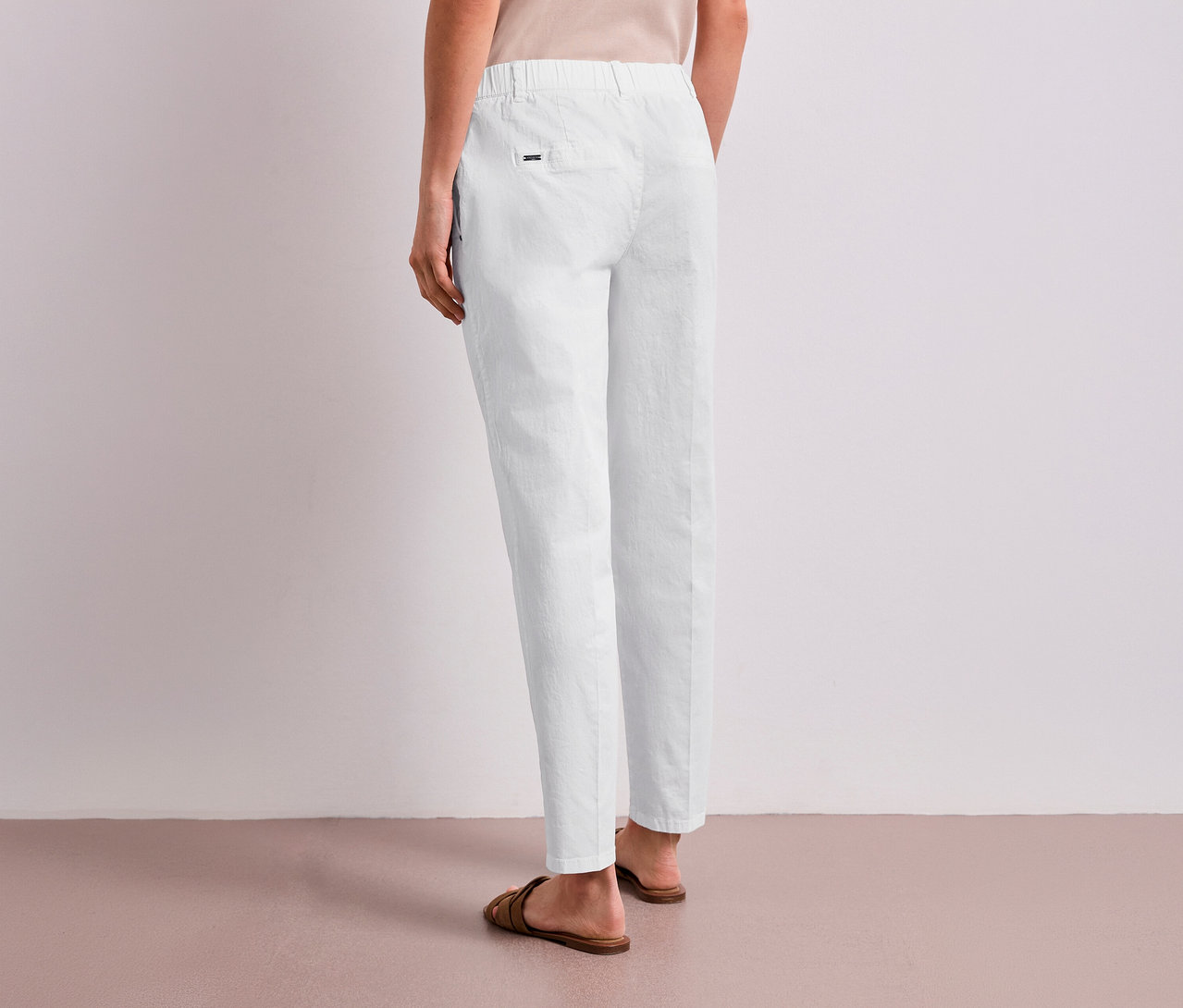 Une personne est debout de dos, portant un chino blanc Street One et des sandales marron.