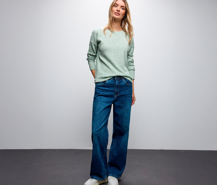 Une femme blonde porte un maillot avec structure Street One, un jean bleu et des baskets blanches.