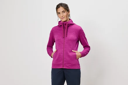 Femme portant un sweat à capuche rose, les mains dans les poches, sur un fond blanc.