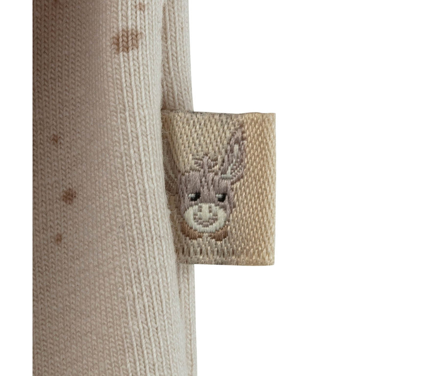 Gros plan d'un tissu tricoté beige avec une petite étiquette carrée beige brodée d'un visage d'âne de dessin animé.