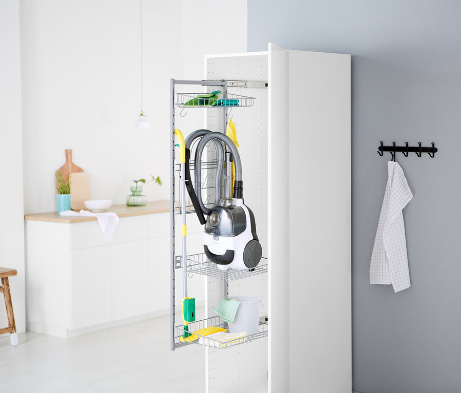Un aspirateur et des produits de nettoyage sont rangés dans un placard blanc ouvert.