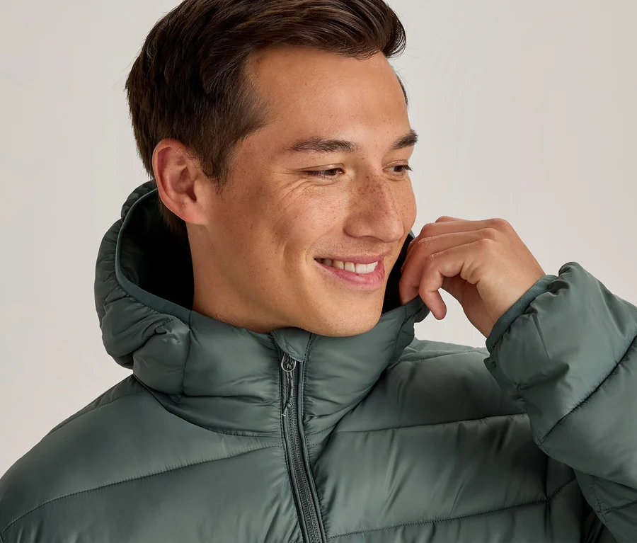 Homme souriant portant une doudoune verte, tenant le col avec sa main droite.