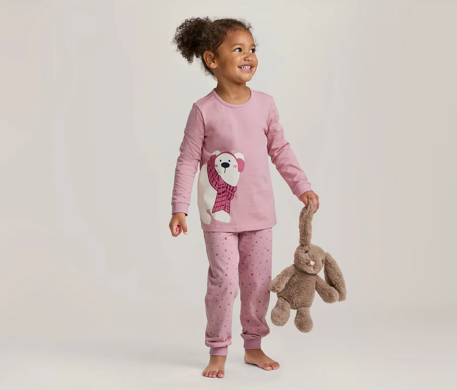 Jeune fille en pyjama rose avec un motif d'ours polaire, tenant un lapin en peluche marron.
