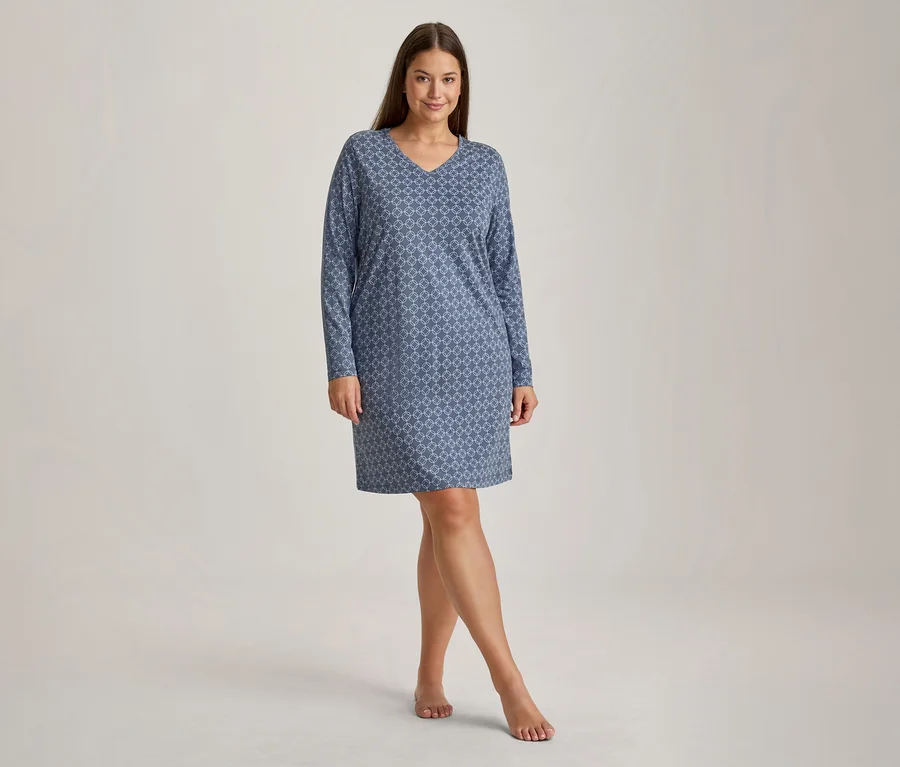 Femme souriante debout pieds nus, vêtue d'une chemise de nuit bleue à motifs, manches longues et col en V.