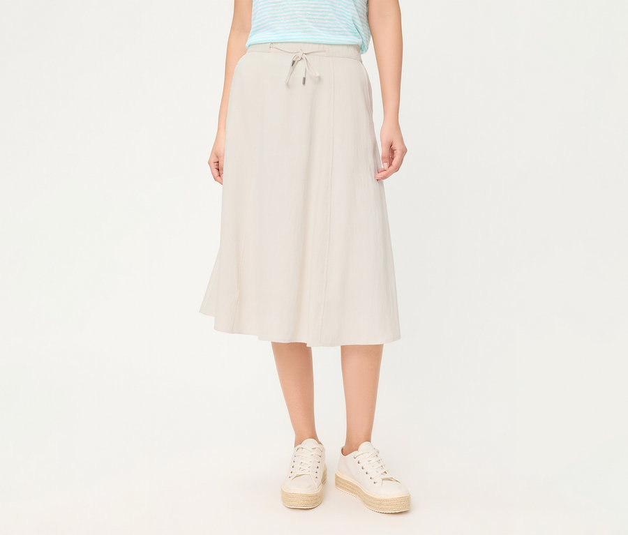 Personne portant une jupe en lin Olsen beige avec cordon de serrage et des baskets compensées blanches.