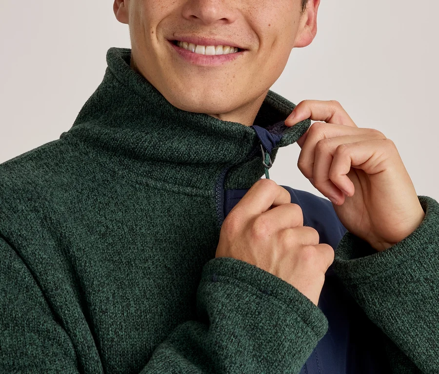 Homme souriant ajustant le col d'une veste polaire texturée verte avec une couche intérieure bleu marine.