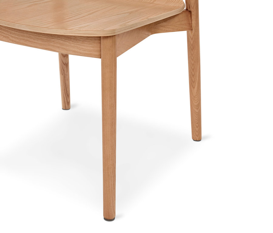Partie inférieure d'une chaise en bois clair avec une assise incurvée et des pieds fins, dotée de capuchons noirs aux pieds, sur fond blanc.