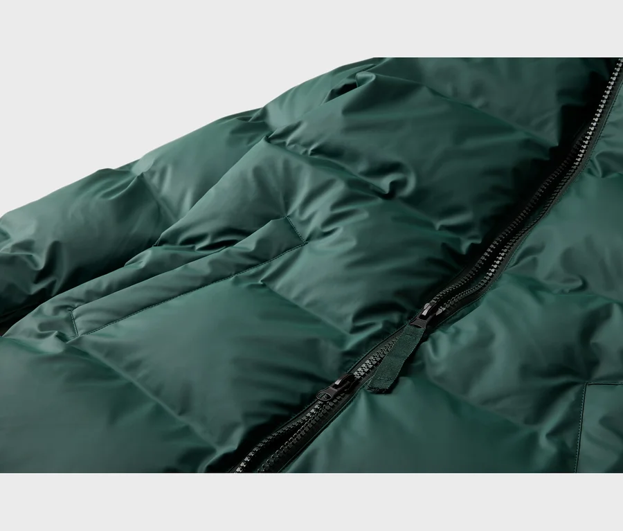 Gros plan d'une doudoune matelassée vert foncé avec une fermeture éclair noire partiellement ouverte en diagonale.