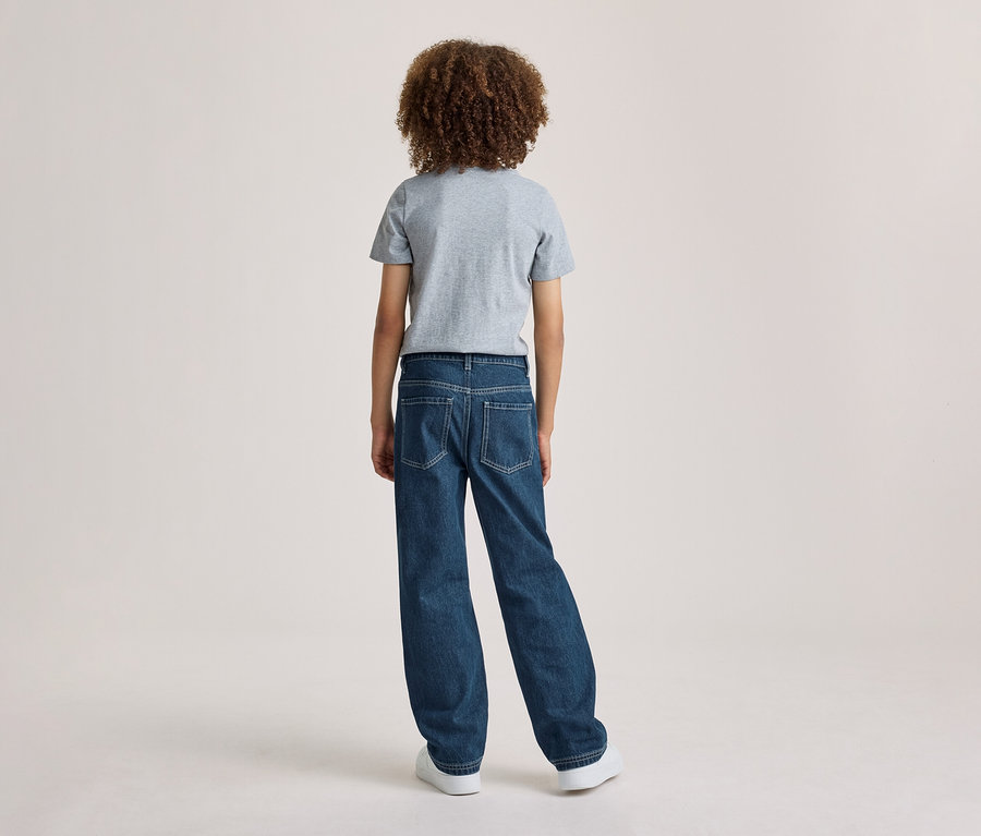 Une personne aux cheveux bouclés, vue de dos, portant un t-shirt gris et un jean bleu.