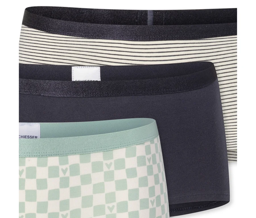 Trois shorts de fille empilés: un rayé, un gris foncé uni et un à carreaux vert clair et blanc avec des cœurs.