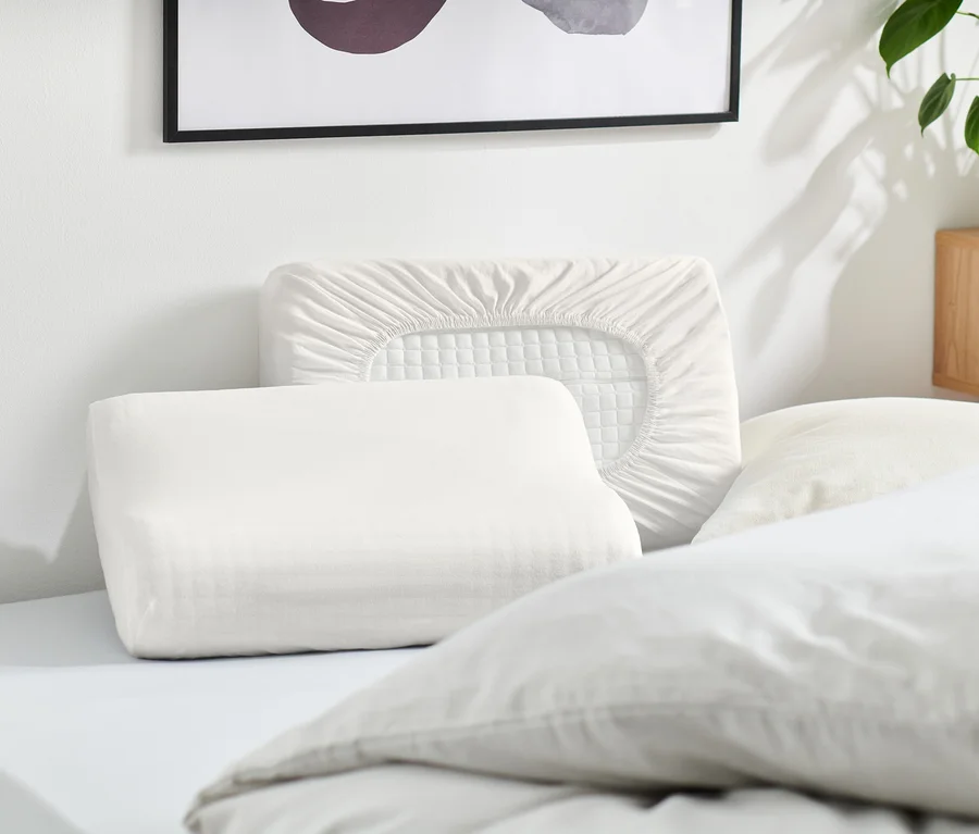 Plusieurs oreillers blancs et une taie d'oreiller blanche sont posés sur un lit.