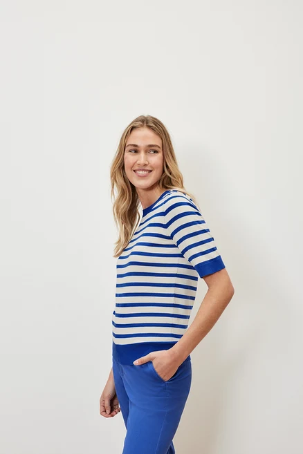 Une femme porte un pull en maille fine rayé et un pantalon bleu.
