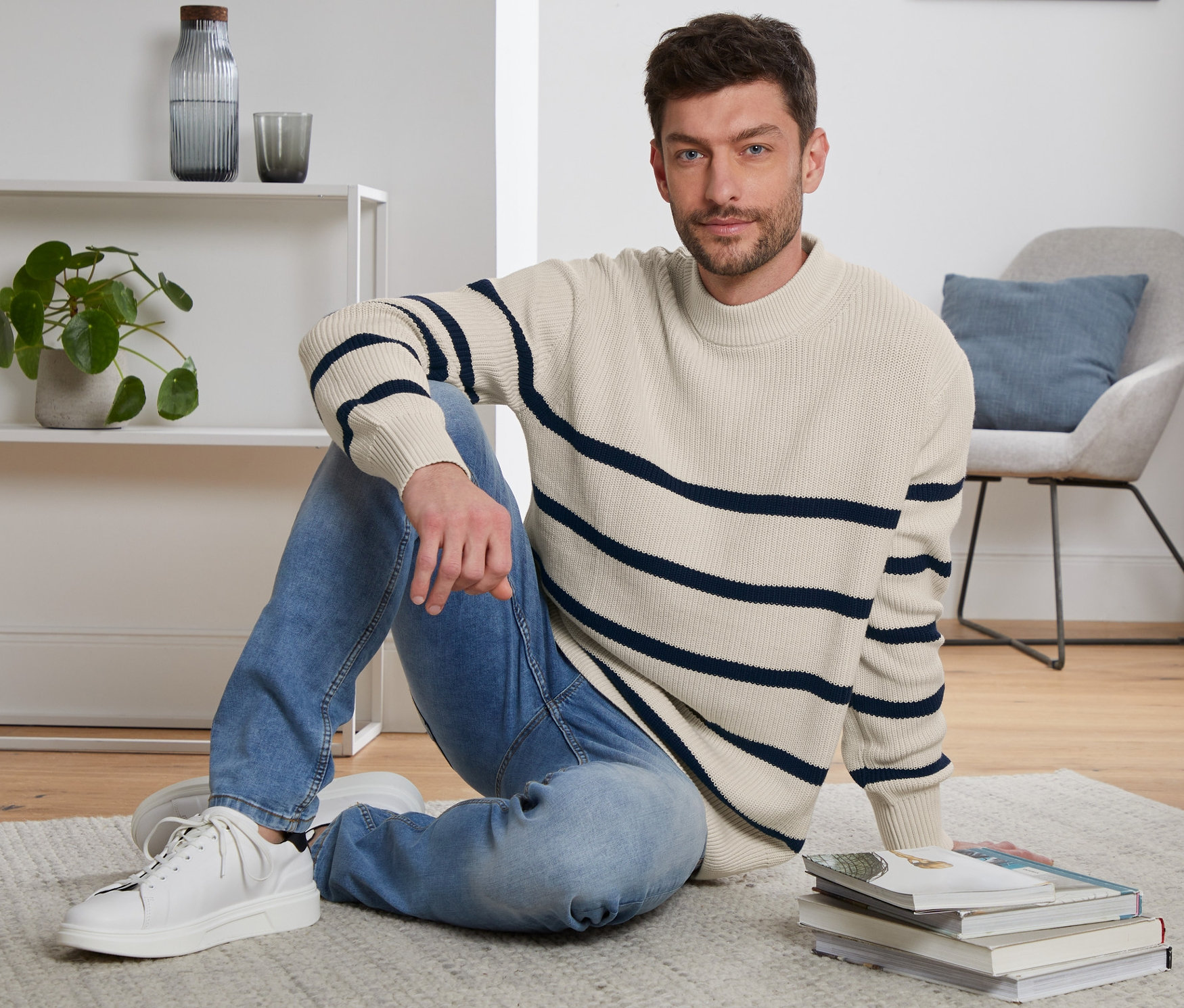 Un homme est assis par terre sur un tapis et porte un pull en maille.