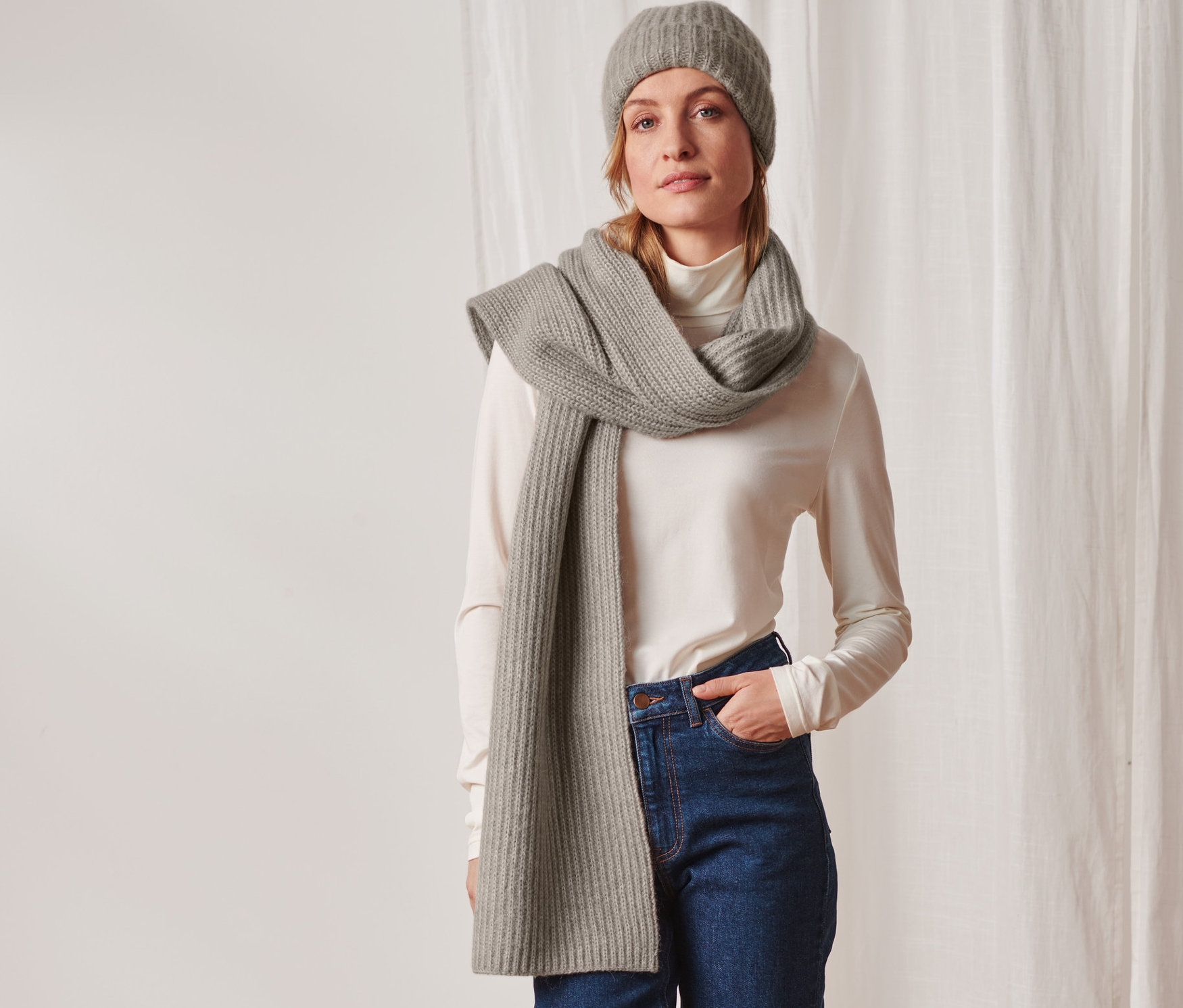 Femme posant avec une écharpe en maille taupe et un bonnet.