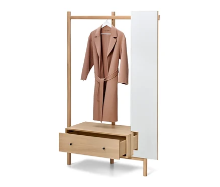 Un manteau marron clair est suspendu à un cintre blanc sur un porte-manteau en bois avec un tiroir ouvert et un miroir.