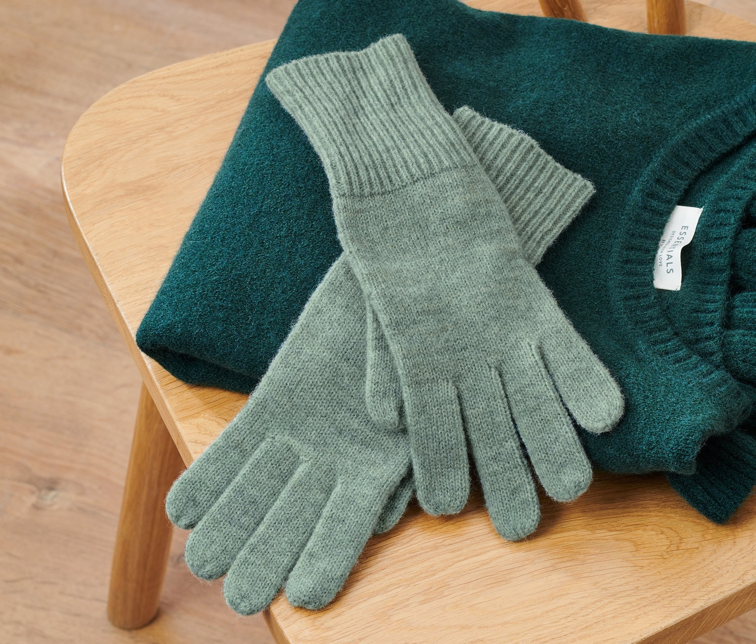 Sur une chaise en bois sont posés un pull vert et des gants en maille avec de la laine, sauge.