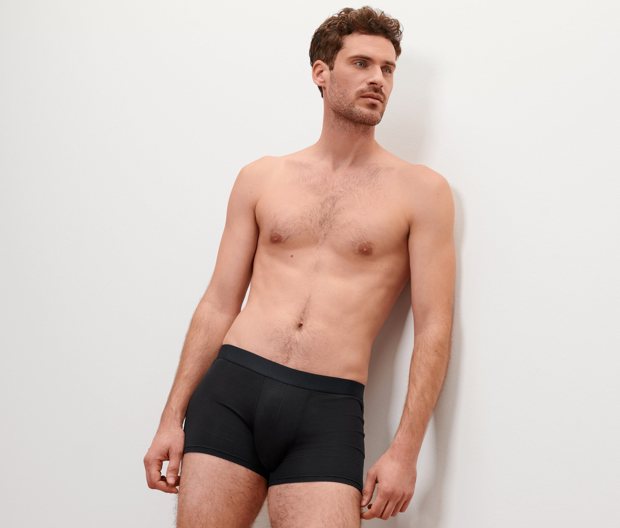 Un homme appuyé contre un mur porte 4 boxers noirs.