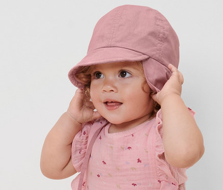 Un enfant ajuste un bonnet d’été rose pour enfant avec indice de protection UV 80.