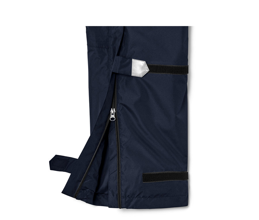 Détail d'un pantalon de pluie unisexe high tech avec fermeture éclair ouverte et détail réfléchissant.