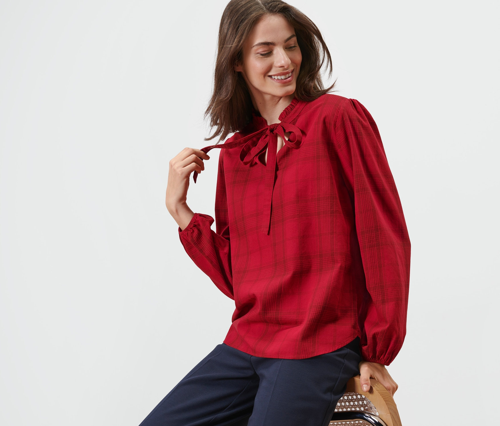 Femme assise sur une chaise portant une blouse à carreaux avec lavallière.