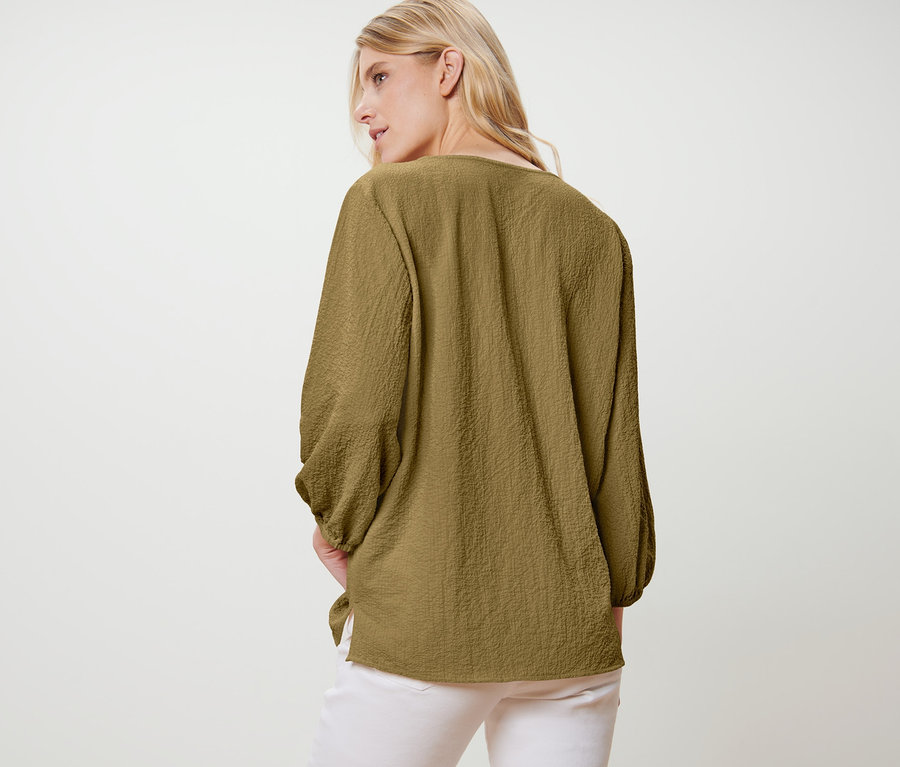 Une femme en chemisier-tunique, dos à la caméra.