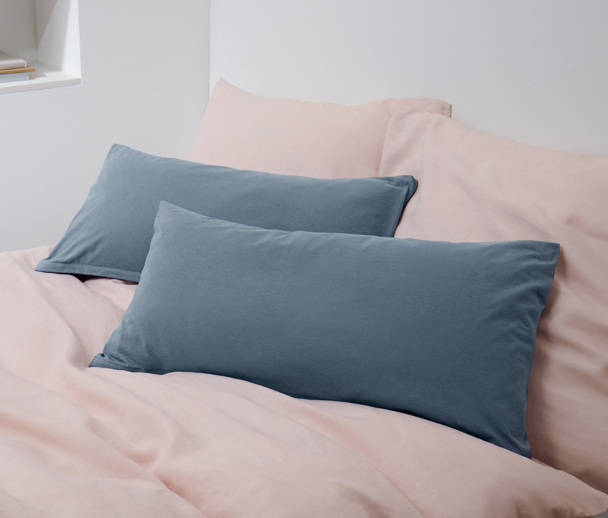 Deux taies d'oreiller en jersey bleues sont posées sur un lit avec du linge de lit rose.