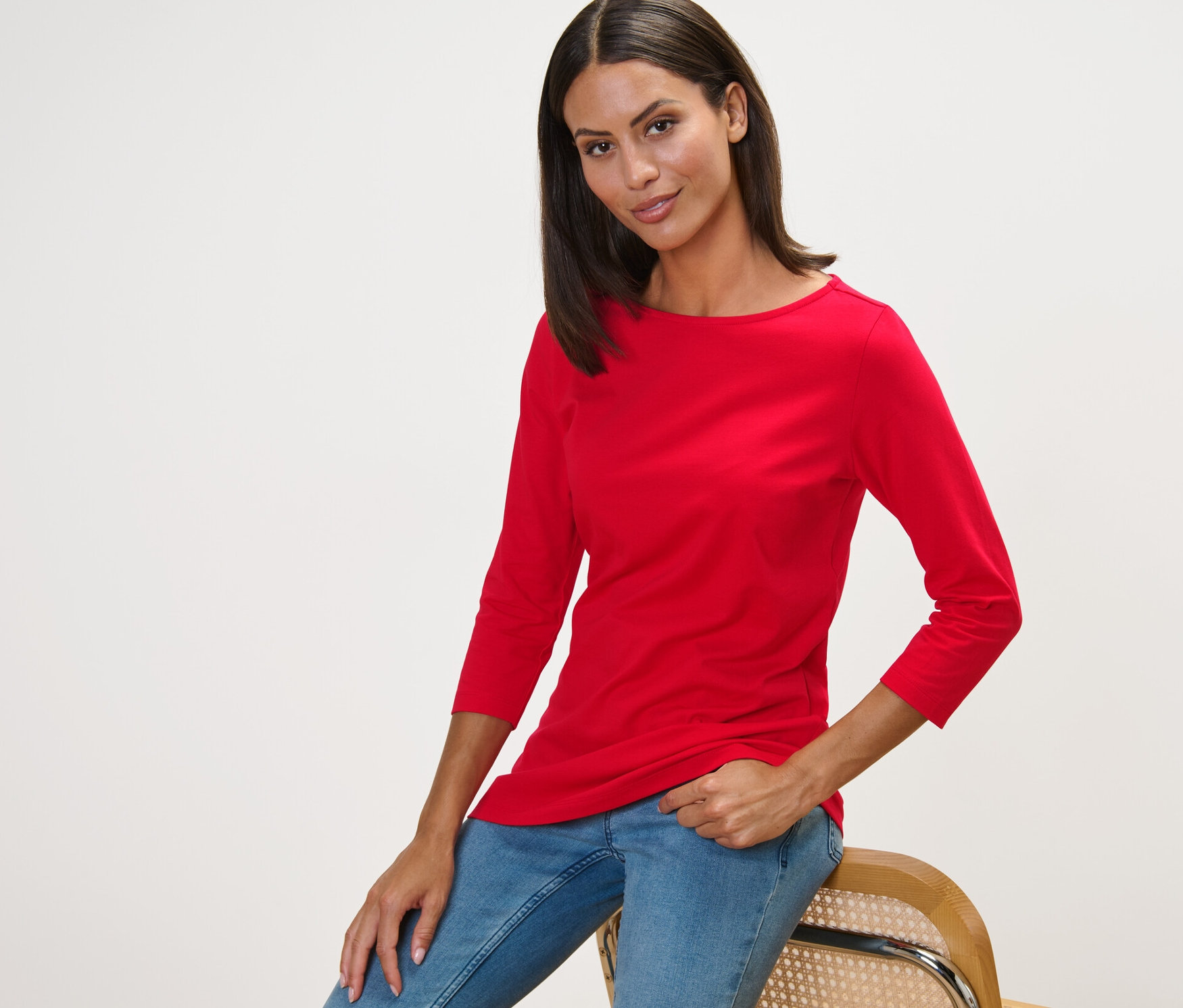Femme assise sur une chaise portant un t-shirt rouge à manches 3/4.