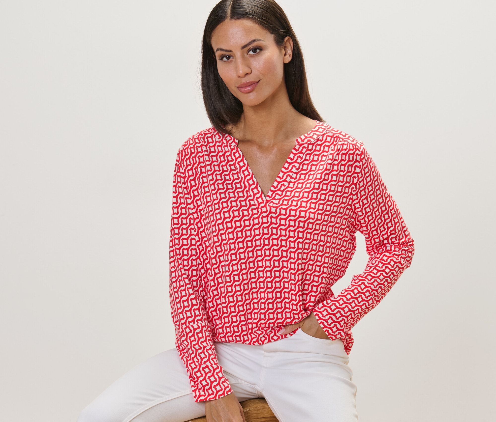 Femme assise sur un tabouret portant une blouse imprimée rouge.