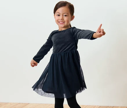 Une fillette souriante en robe en tulle pose sur un fond clair.