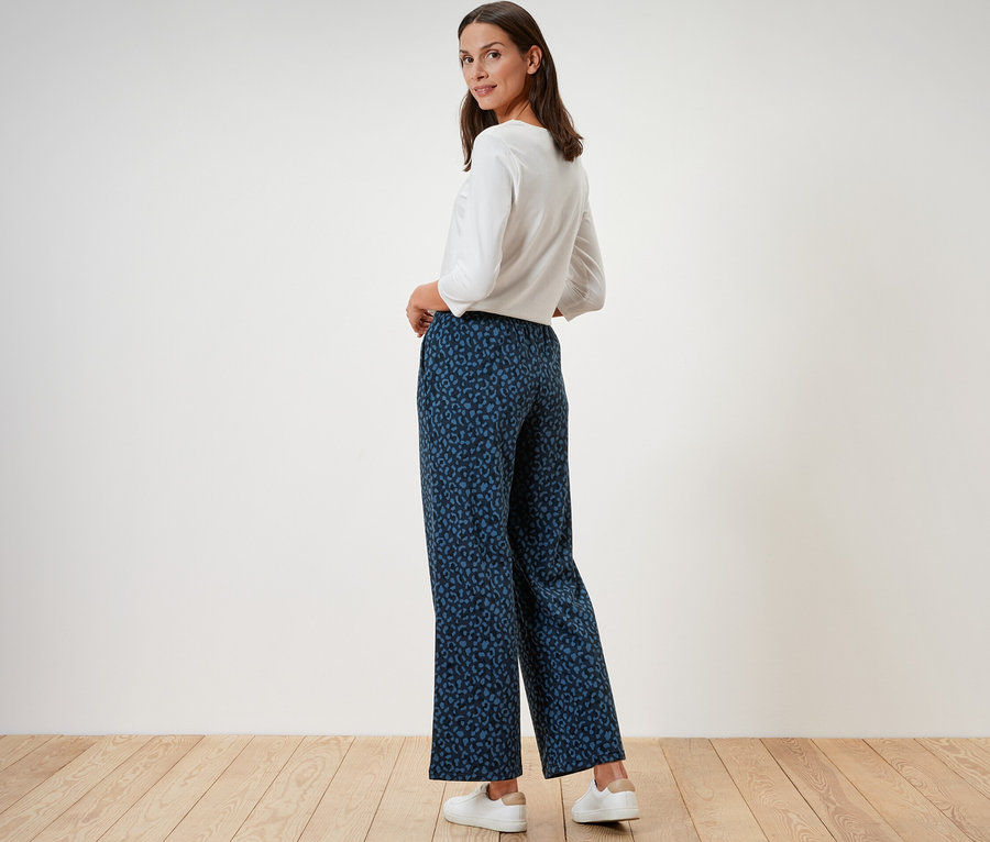 Femme posant en pantalon doux imprimé et haut blanc.