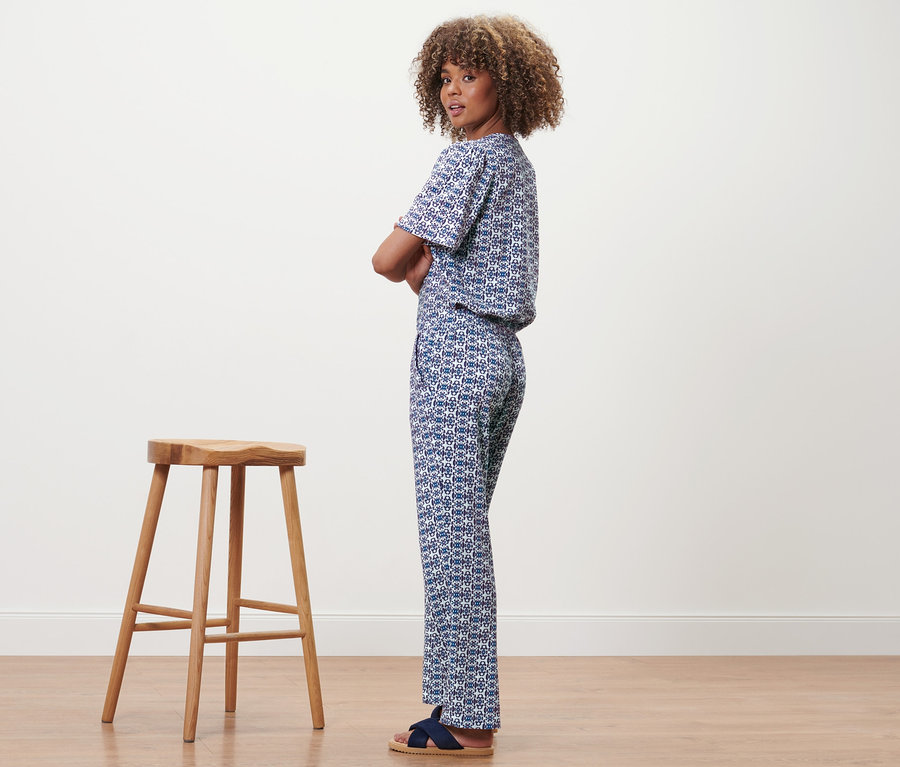 Une femme portant un pantalon à imprimé intégral se tient à côté d'un tabouret en bois.