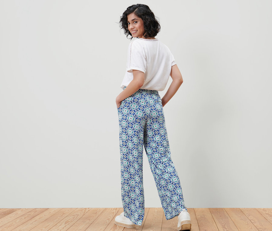 Femme souriante posant dans un pantalon palazzo à imprimé intégral et un haut blanc.