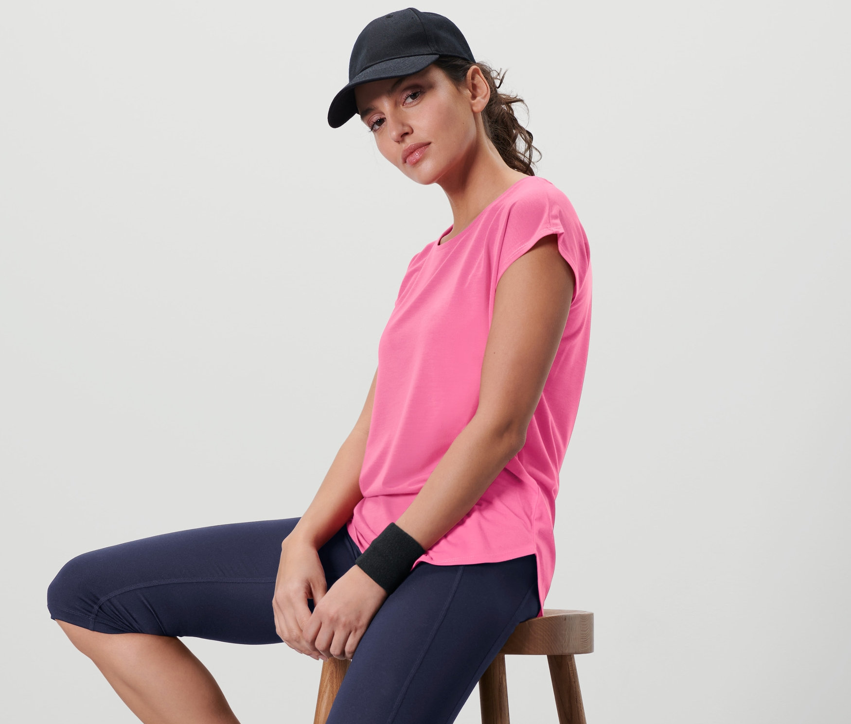 Femme assise sur un tabouret portant un t-shirt de sport rose vif.