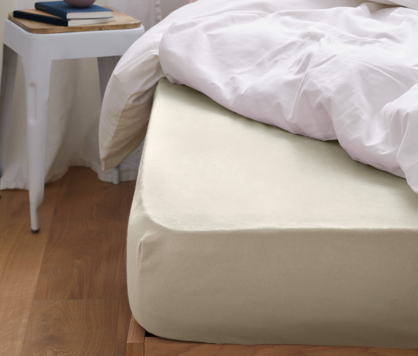 Un drap-housse en molleton crème sur un lit avec des couvertures blanches et un oreiller rose.
