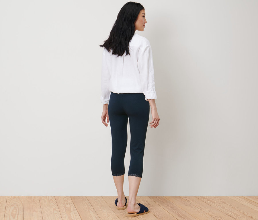 Une femme se tient dos à la caméra et porte un legging 3/4 bleu foncé avec une bordure en dentelle.