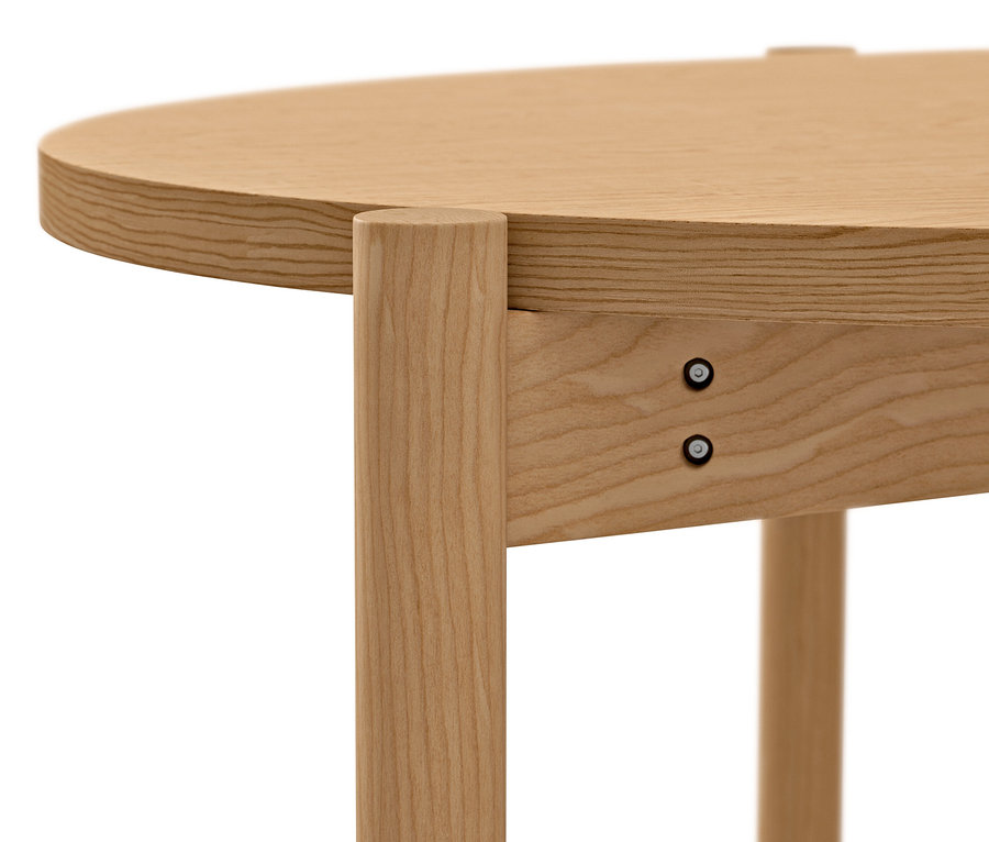 Gros plan d'une table basse ronde en bois clair avec des vis apparentes.