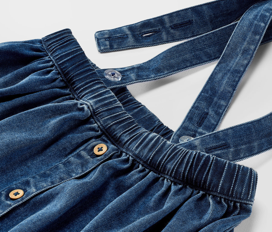 Gros plan d'une jupe en denim pour tout-petit avec bretelles et boutons.