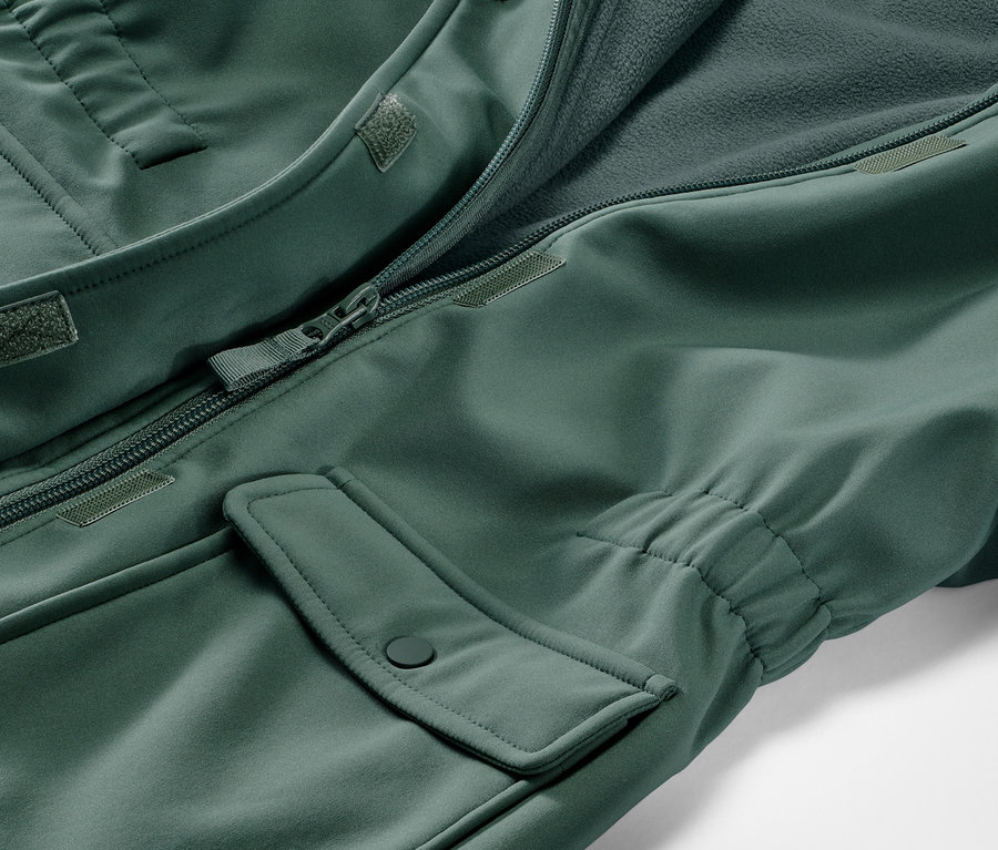 Gros plan sur un manteau en softshell pour enfant vert avec une fermeture éclair ouverte et une poche.