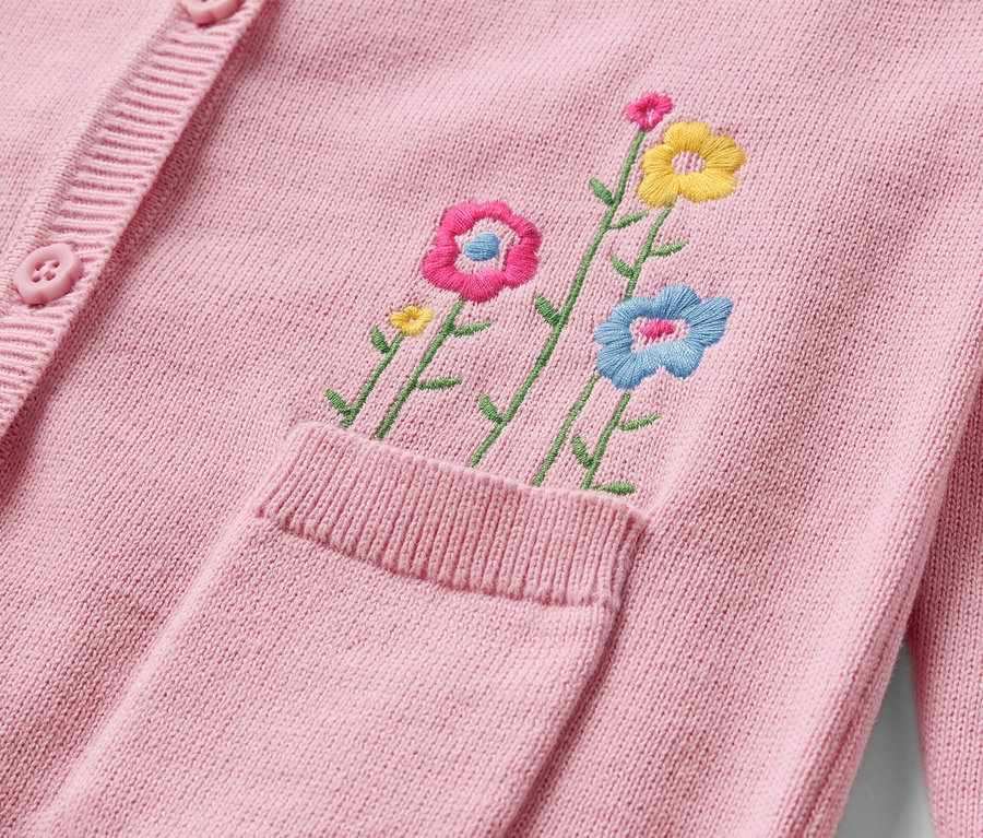Détail d'une jaquette en maille rose pour bébé avec broderie florale et boutons.