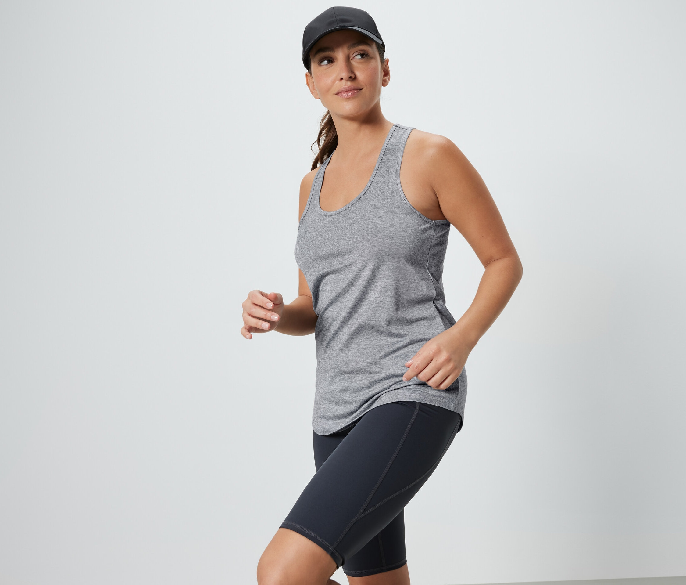 Femme portant un débardeur gris et un short de cycliste noir avec une casquette. 2 tops techniques, noir et gris.
