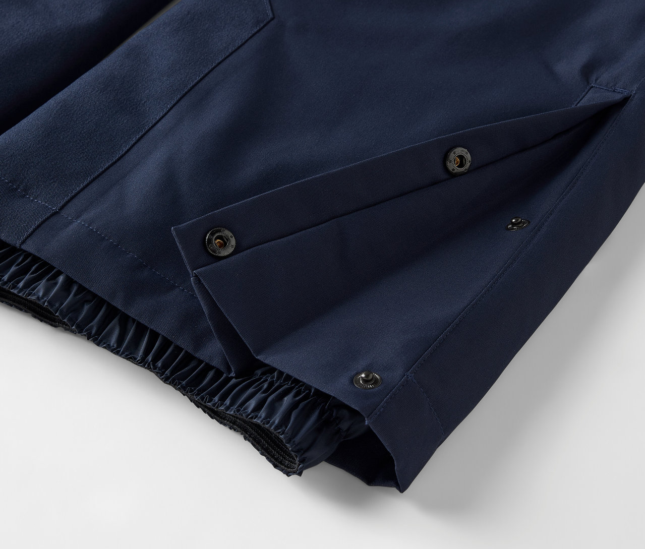 Détail d'un pantalon bleu avec fermeture à boutons-pression et ourlet élastique.