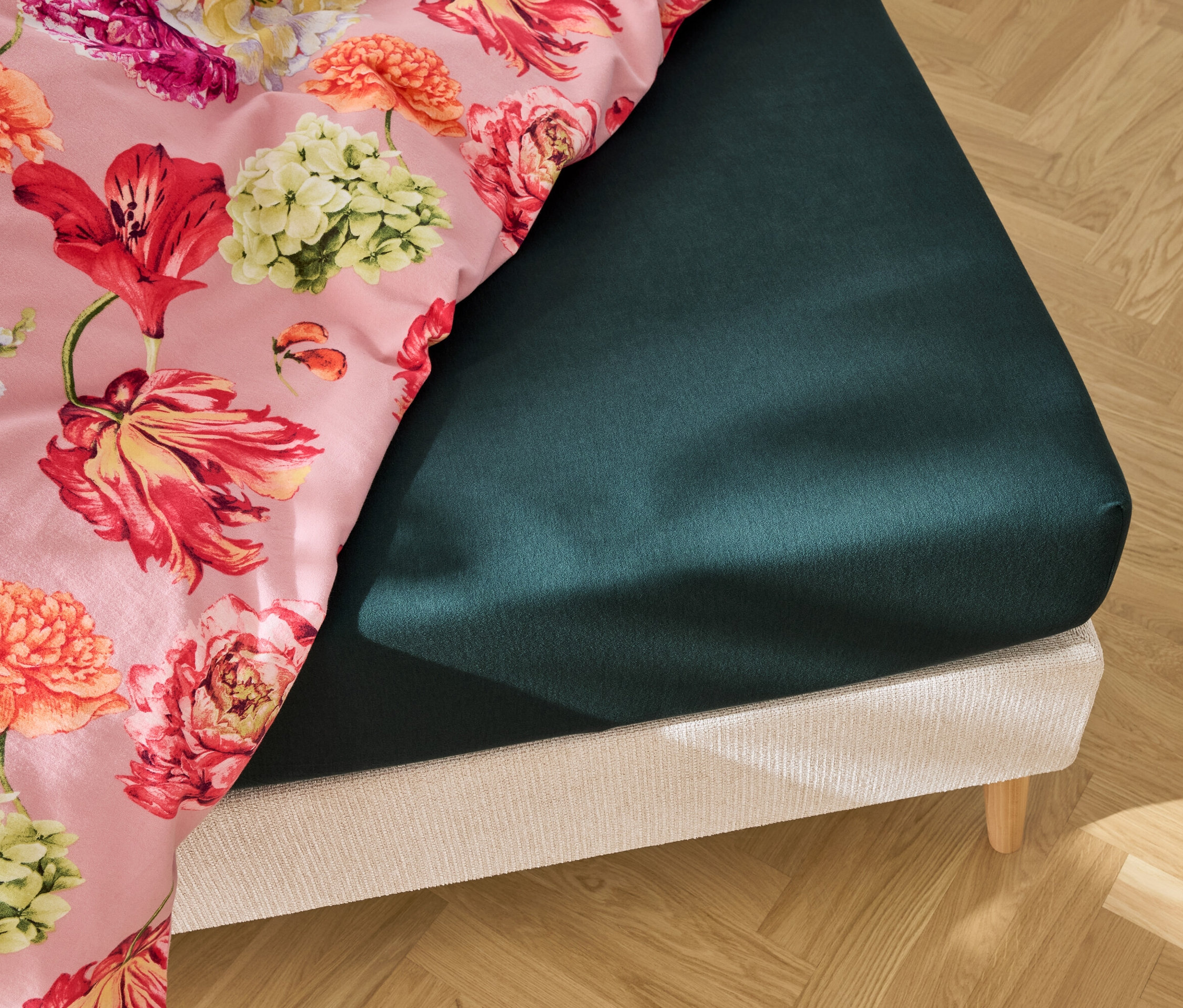 Vue détaillée d'un lit avec un drap-housse vert foncé et une literie à imprimé floral.