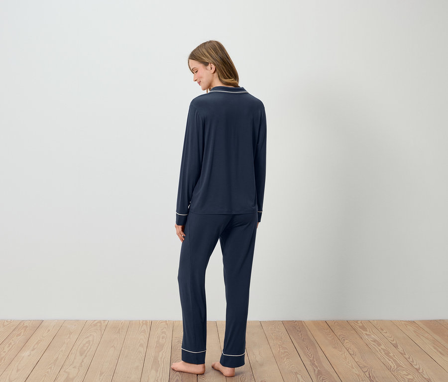 Une femme, vue de dos, porte un pyjama bleu marine avec des finitions blanches.