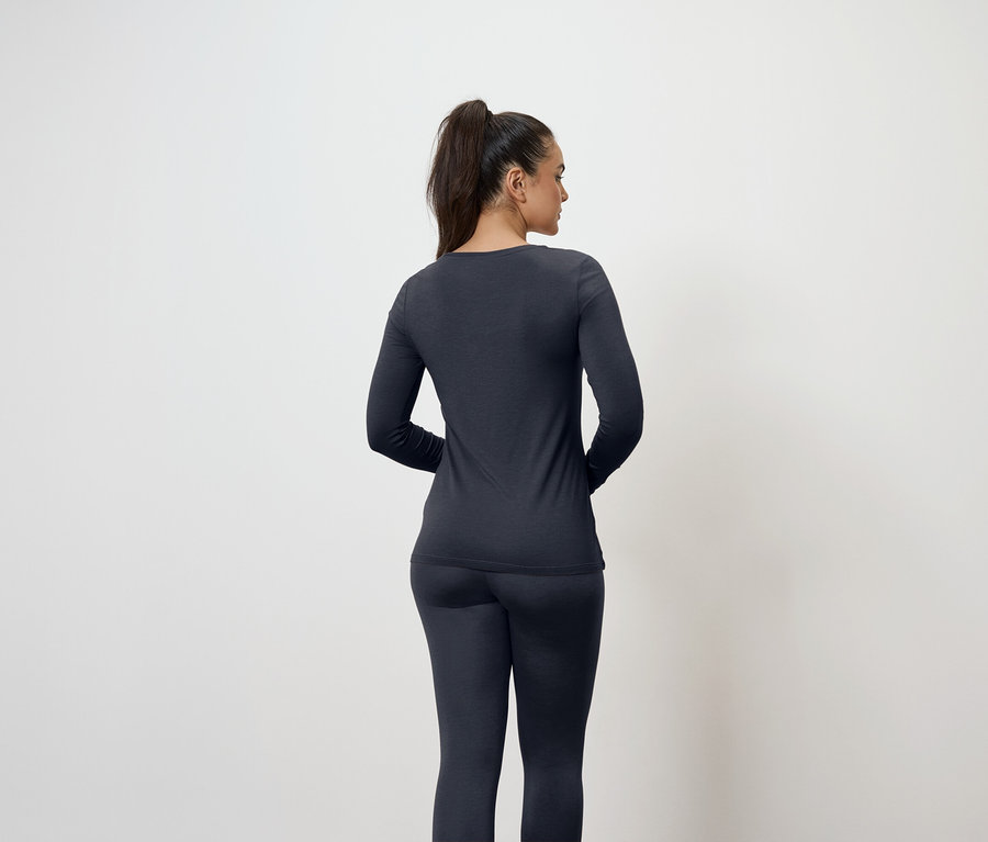 Une femme vue de dos, les cheveux attachés, porte un haut à manches longues bleu foncé et un legging.