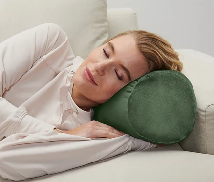 Une femme dort sur un canapé avec un coussin cylindrique sous la tête.