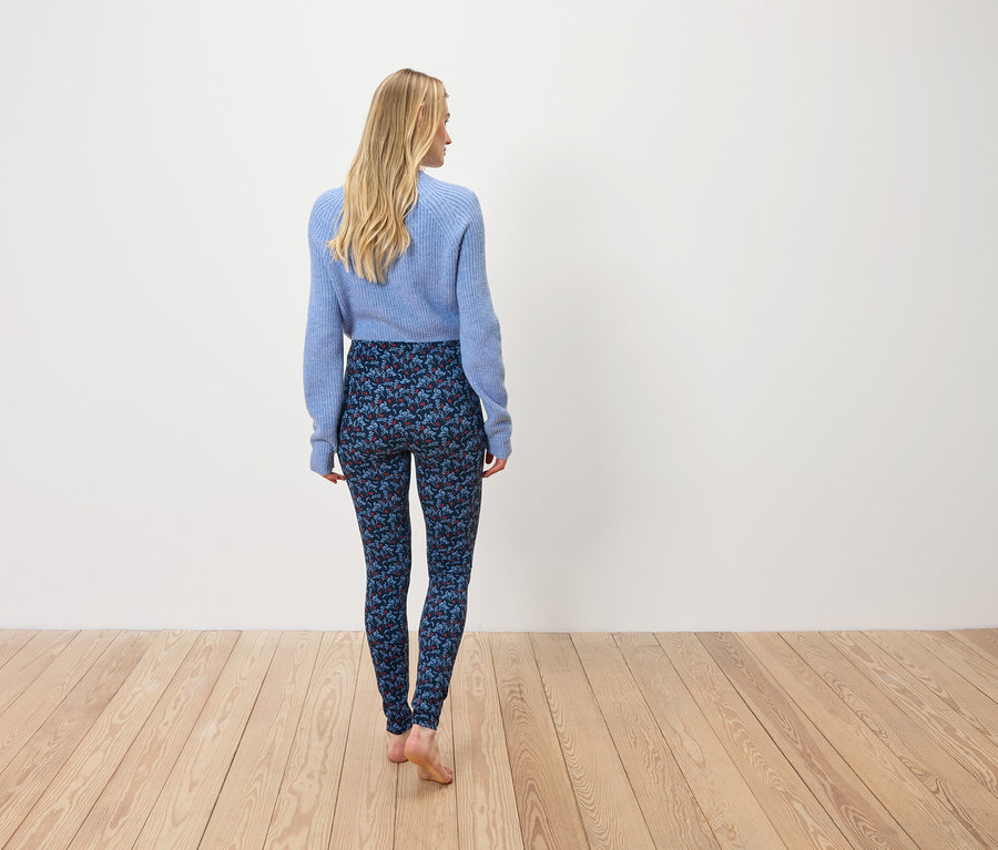 Une femme en pull bleu et leggings à motifs se tient dos à l'appareil photo.