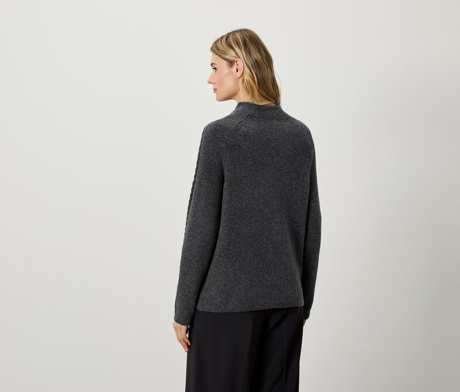 Une femme, dos à la caméra, porte un pull gris foncé et un pantalon noir.