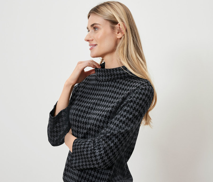 Une femme blonde pose dans un haut gris à motif pied-de-poule.