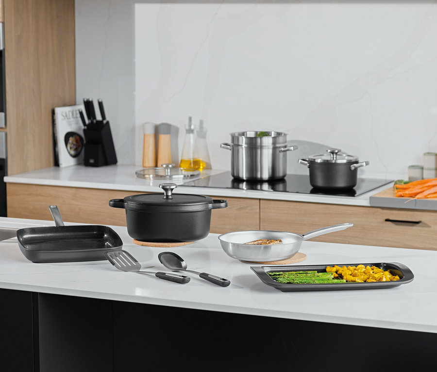 Diverses casseroles, poêles et ustensiles de cuisine sur un comptoir de cuisine blanc.