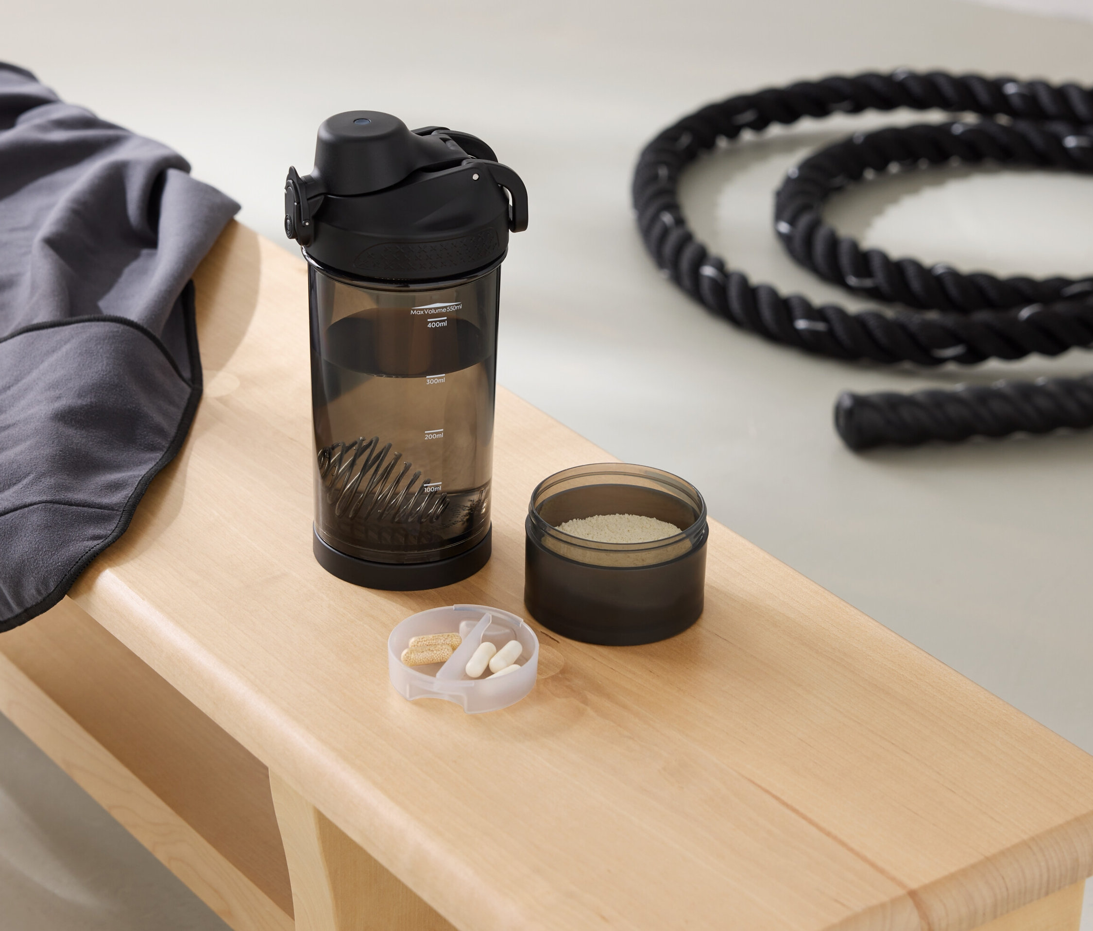 Un sweat-shirt gris, une gourde, une boîte de poudre et une corde sont posés sur un banc.